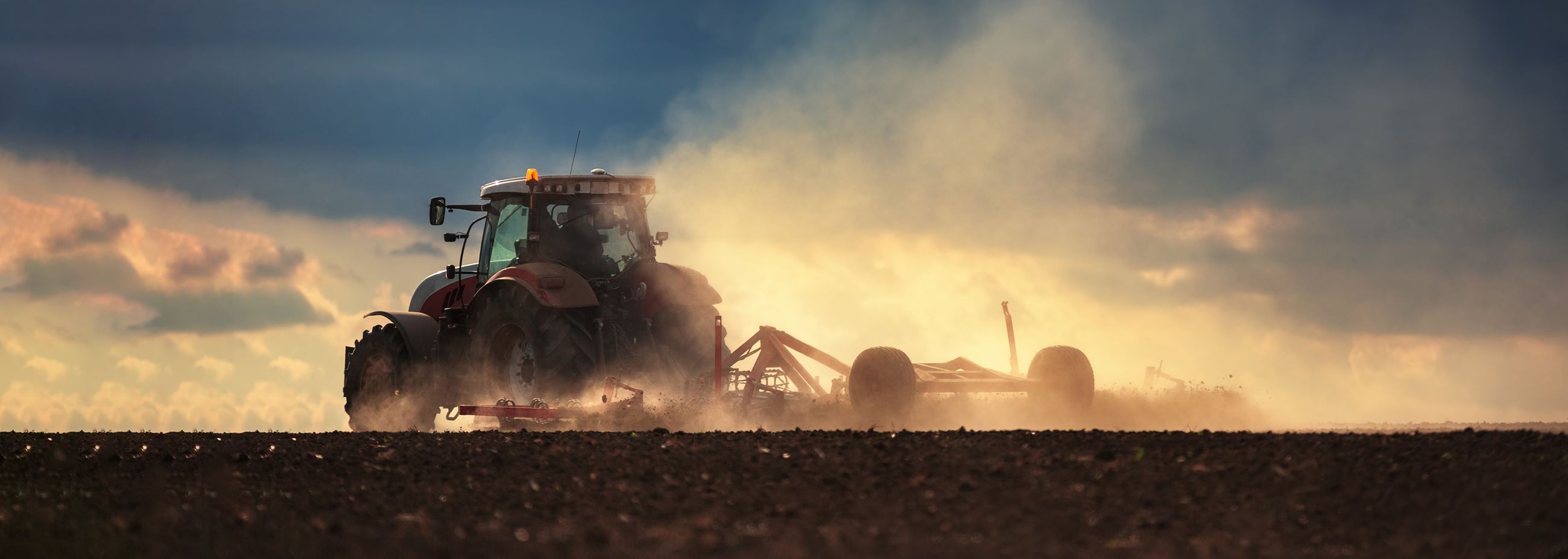 Farmer in tractor preparing land with seedbed cultivator, sunset shot